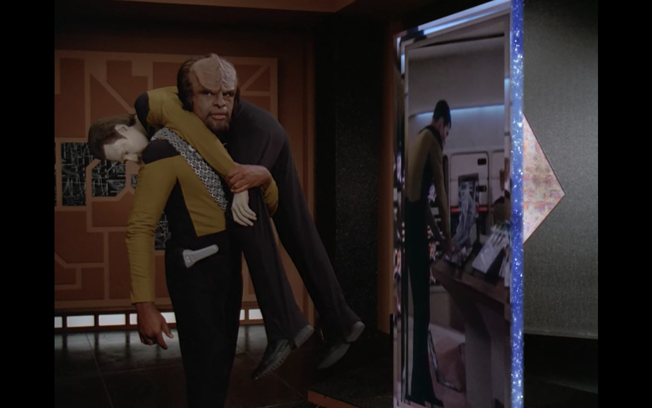 Worf carrying Data in a fireman's hold, facing a strange doorway picturing the Enterprise bridge