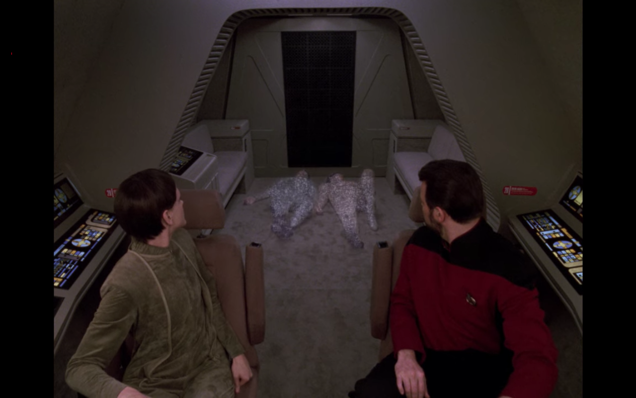 Riker and an alien pilot in a shuttle, looking as two prone figures beam aboard
