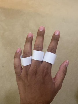 3 white paper rings on the ring, middle, and index fingers of the back of a left hand.