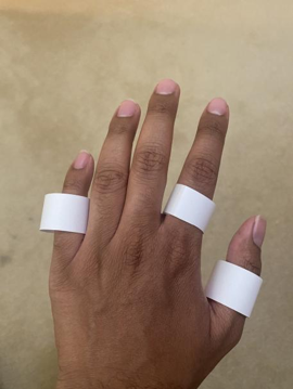 3 white paper rings on the pinky finger, index finger, and thumb of the back of a left hand.