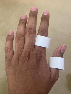 2 white paper rings on the index finger and thumb of the back of a left hand.