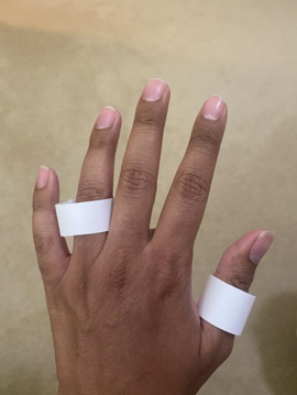 2 white paper rings on the ring finger and thumb of the back of a left hand.