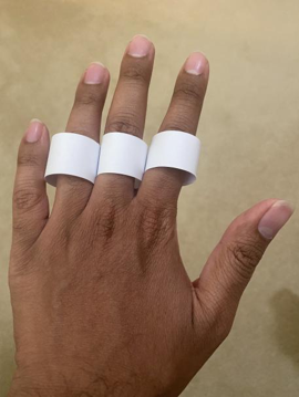 3 white paper rings on the ring, middle, and index finger of the back of a left hand.