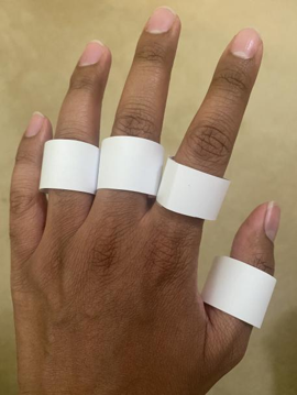 4 white paper rings on the ring, middle, and index fingers and thumb of the back of a left hand.