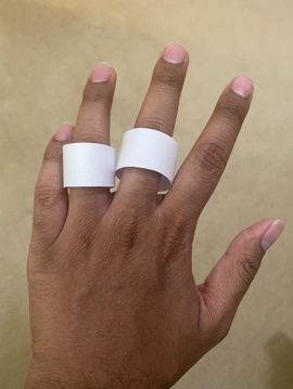 2 white paper rings on the ring and middle fingers of the back of a left hand.