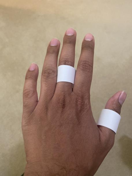2 white paper rings on the middle finger and thumb of the back of a left hand.