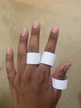 3 white paper rings on the middle finger, index finger, and thumb of the back of a left hand.