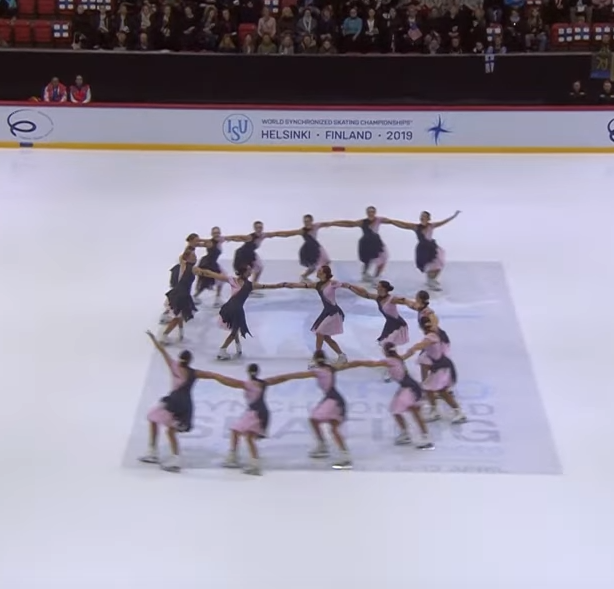 A synchronized skating team forms the letter S.